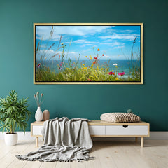 Golden-framed nature canvas print of grassy land with flowers and sea view under clear sky, designed for airy and calm home interiors